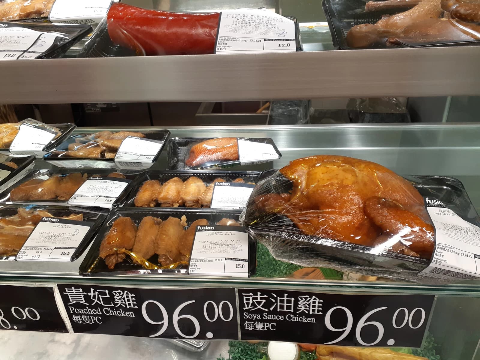 Cooked whole chicken and chicken pieces in plastic packaging on a supermarket shelf.
