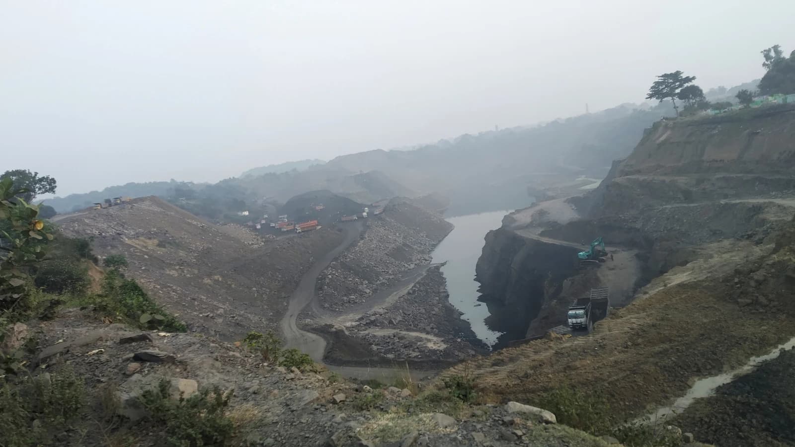 Aerial view of an active open-pit coal mine with heavy machinery and water bodies.
