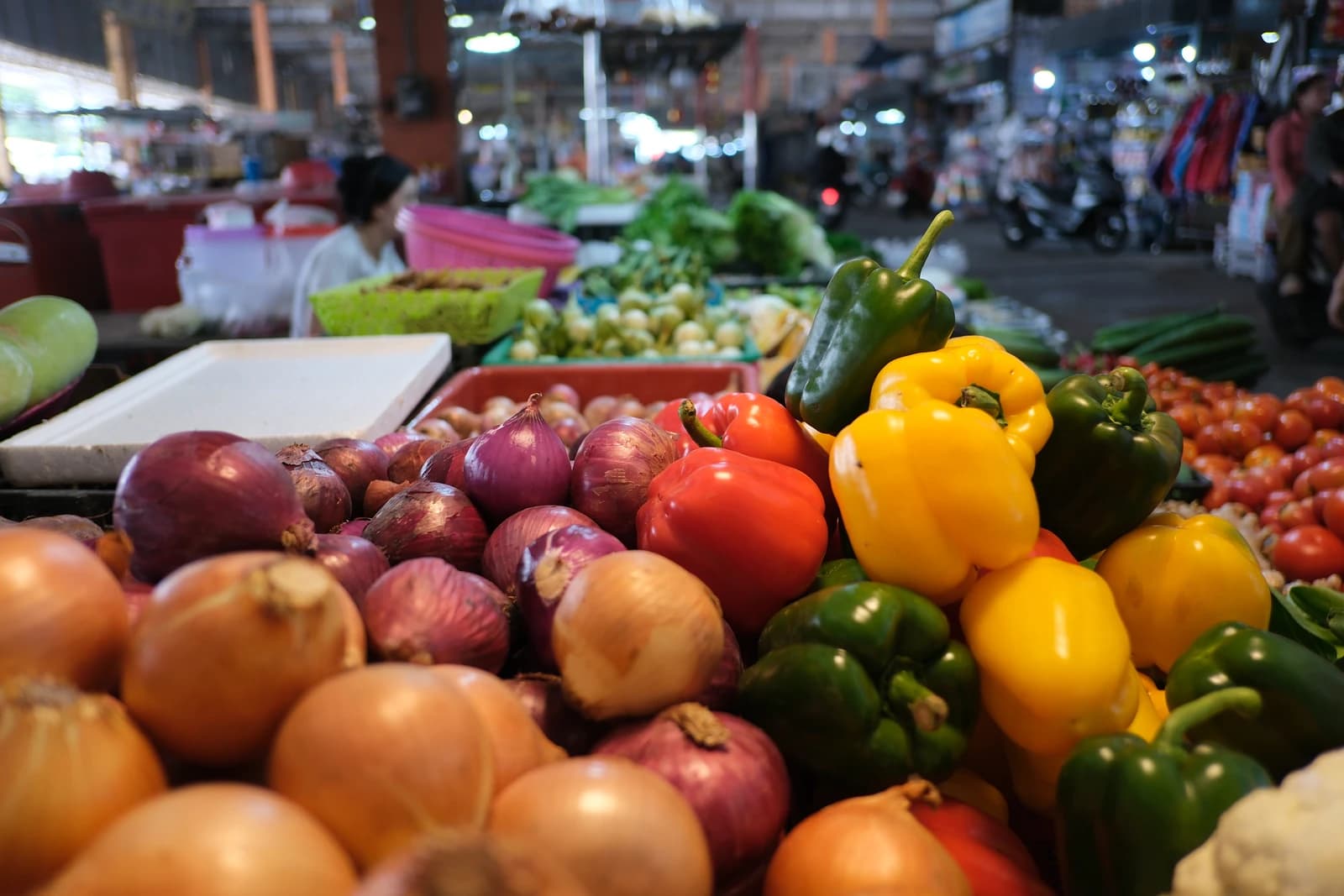 Colorful market stall piled high with fresh onions, red and yellow bell peppers.
