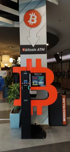 A Bitcoin ATM machine stands prominently within a shopping center.