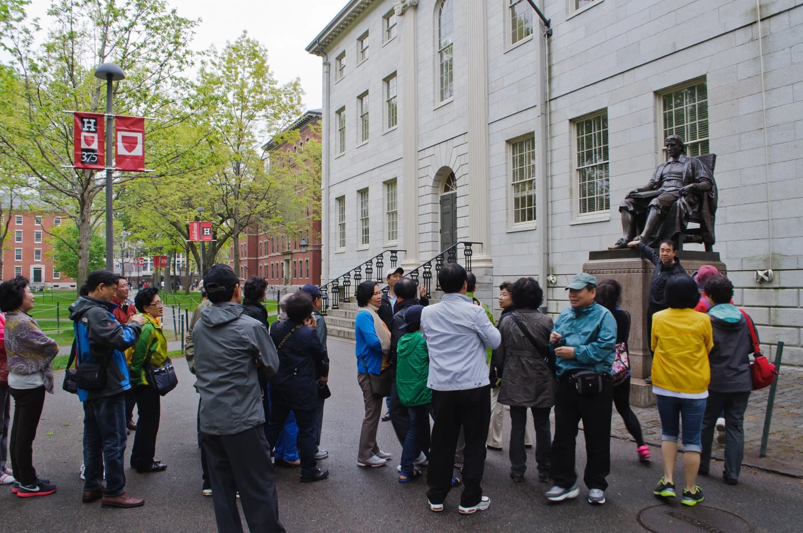 Group of tourists standing near the John Harvard statue in front of a building at Harvard University.