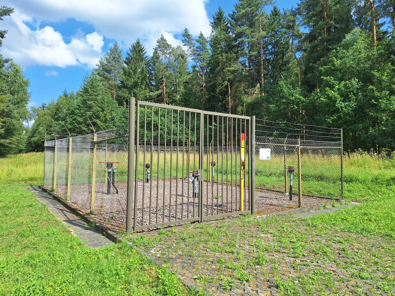 EGL 401 valve station secured with a fence and barbed wire in a wooded area.