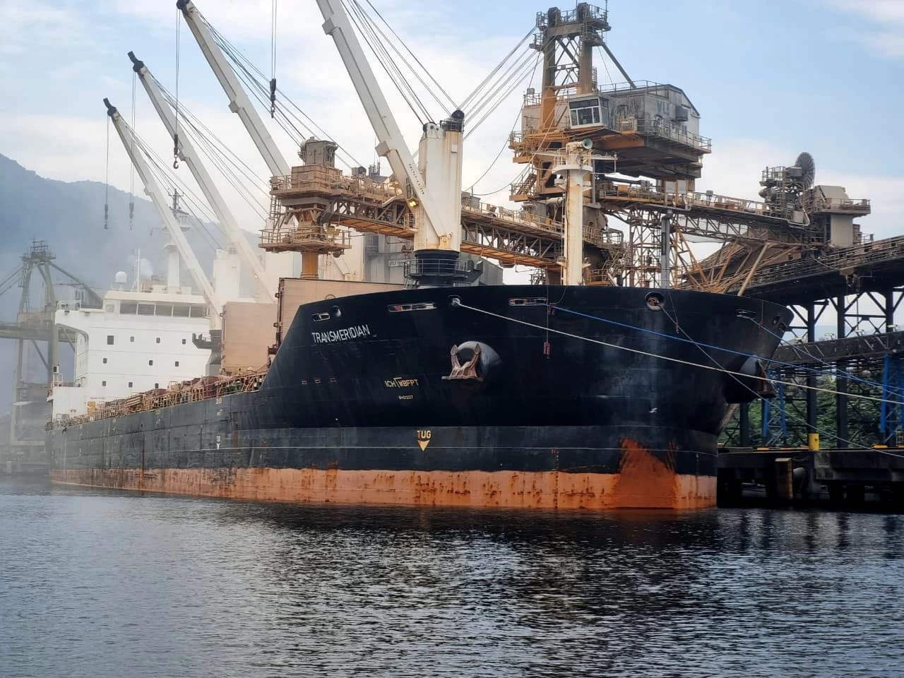 Cargo ship Transmeridian docked at the Port of Santos, with cranes loading goods.