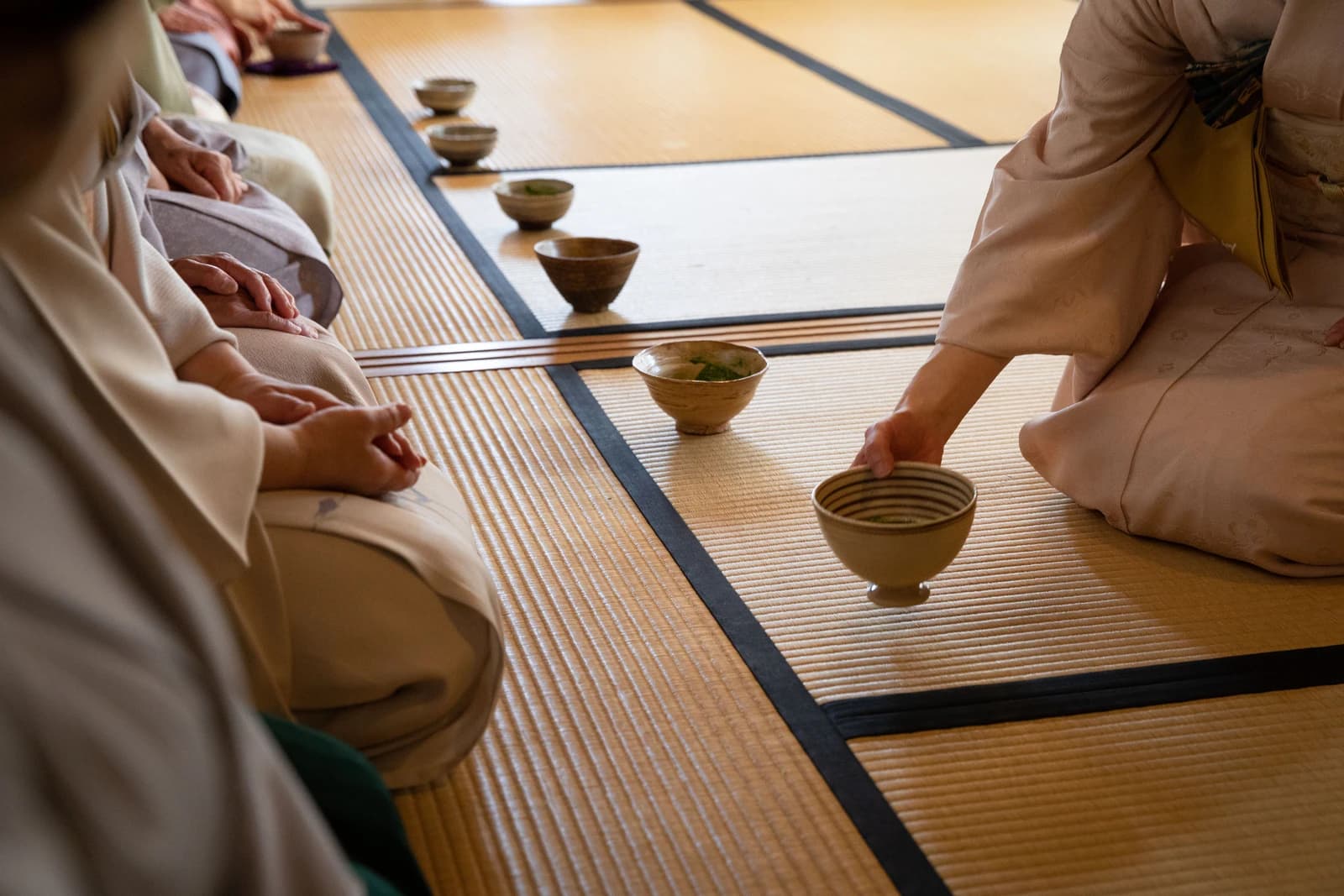 People attending a Japanese tea ceremony, seated on tatami mats with bowls.
