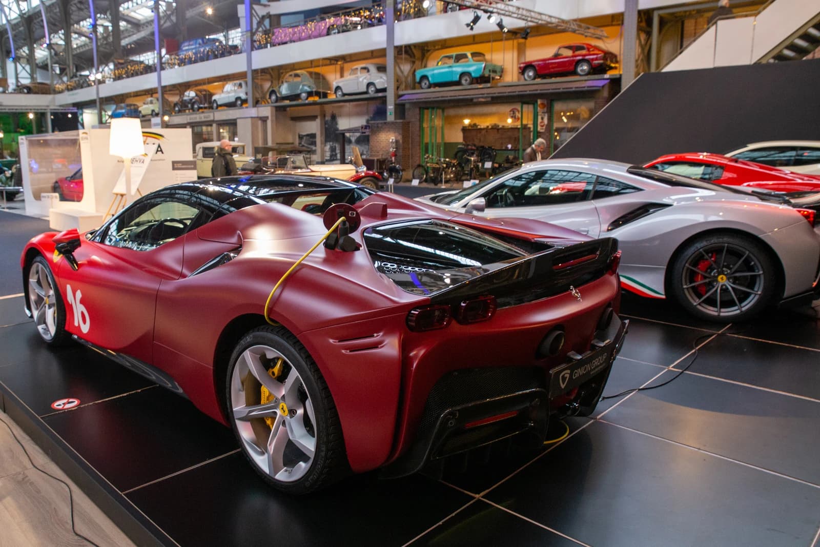 Red Ferrari SF90 Spider on display, connected to a yellow charging cable.