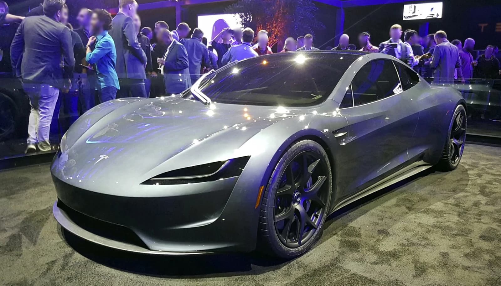 Gray Tesla Roadster 2020 prototype on display with people in the background.