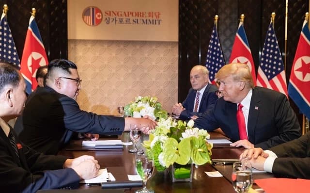 Kim Jong-un and Donald Trump shaking hands across a table at a summit meeting.