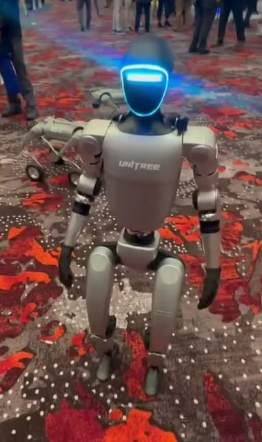 Unitree G1 humanoid robot with glowing blue face standing on a patterned carpet.