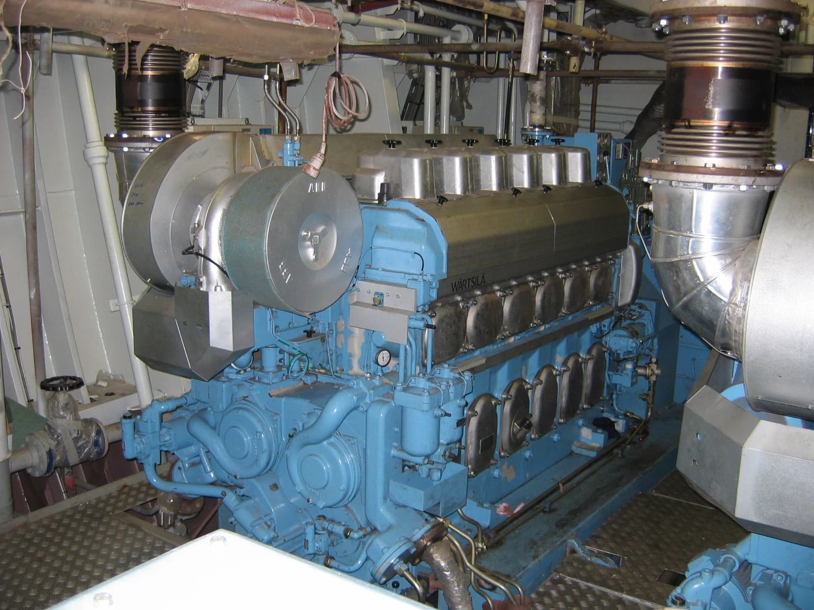 A large blue Wärtsilä 6L20 engine with exposed components in an industrial setting.
