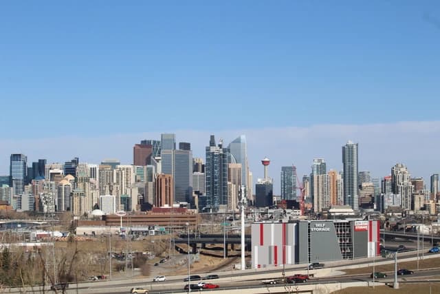 Calgary skyline with skyscrapers, roads, and the Calgary Tower against a blue sky.
