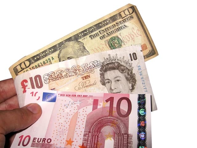 A hand holding a ten dollar bill, a ten pound note, and a ten euro note.