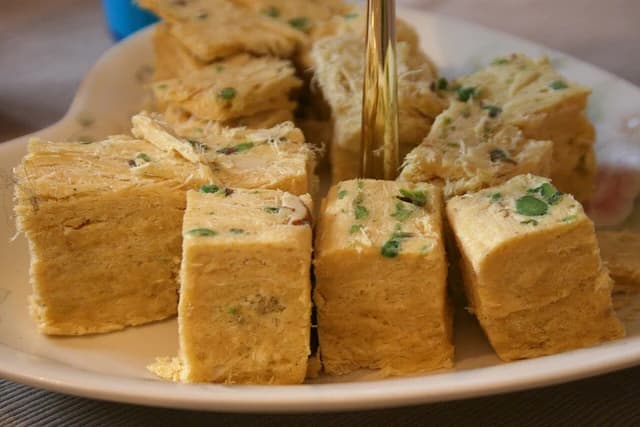 Close-up of golden brown soan papdi, an Indian sweet, on a white plate.