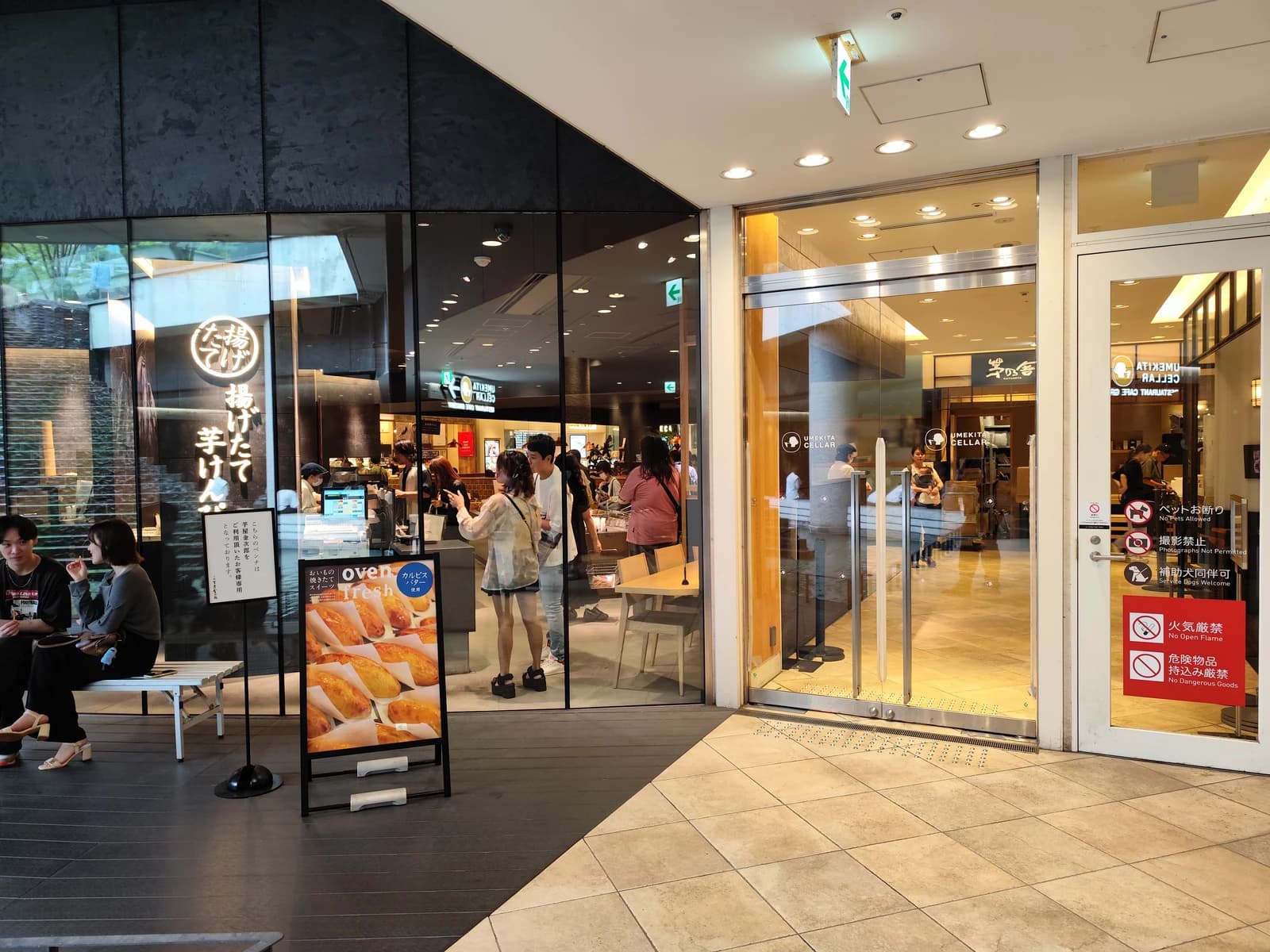 People walking and sitting near storefronts at Grand Front Osaka shopping mall in Osaka, Japan.