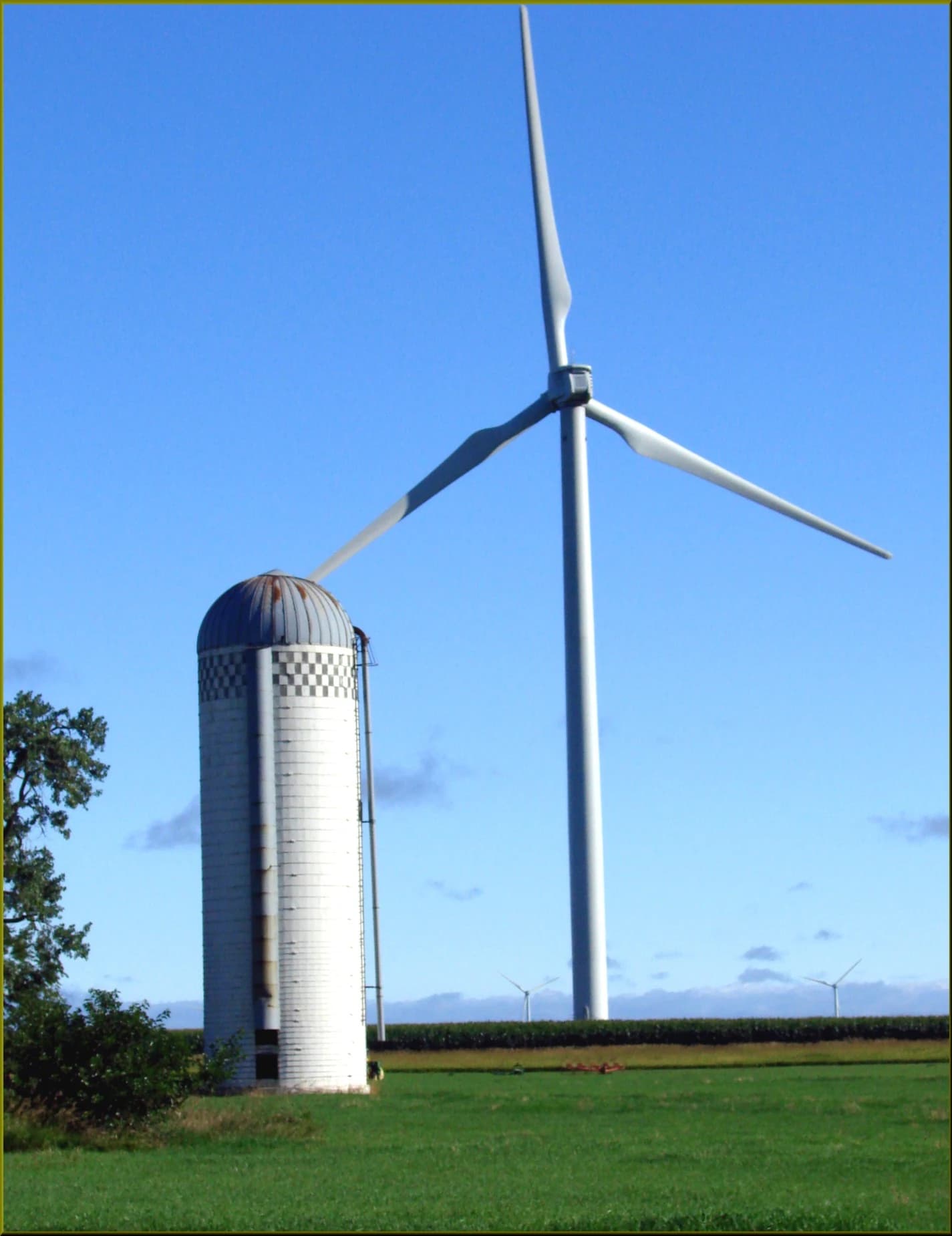 A large wind turbine stands in a green field next to a tall white silo.