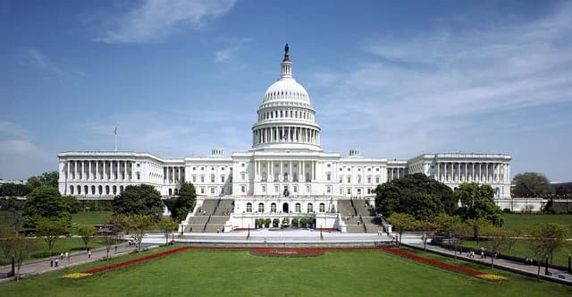 The United States Capitol building, west facade, with green lawns and trees in front.