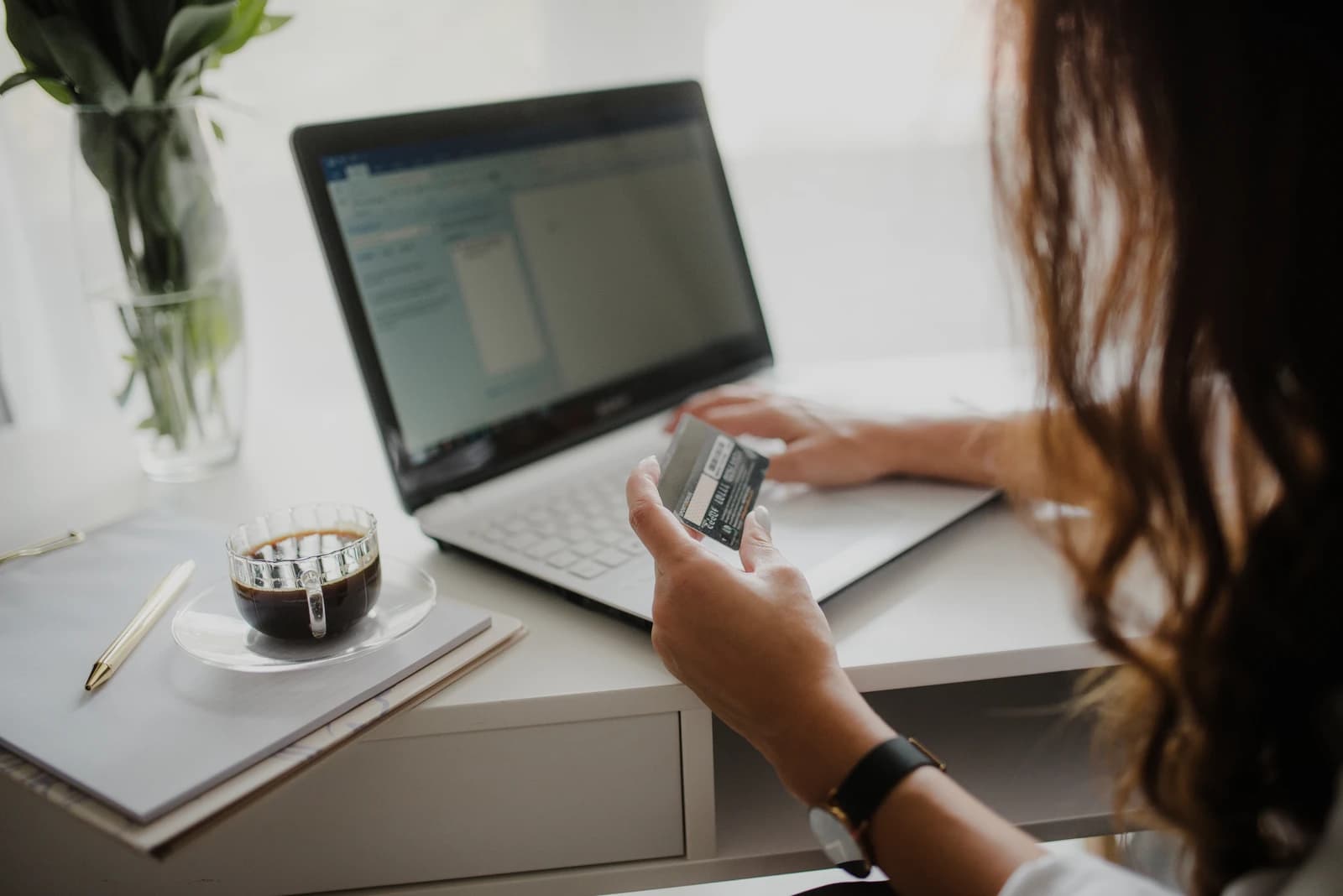 Woman holding a credit card while typing on a laptop computer at a desk.