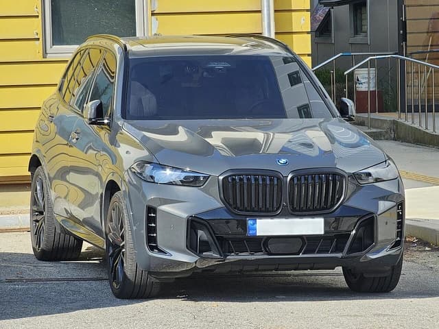 Gray BMW G05 LCI X5 xDrive50e M Sport parked in front of a building.