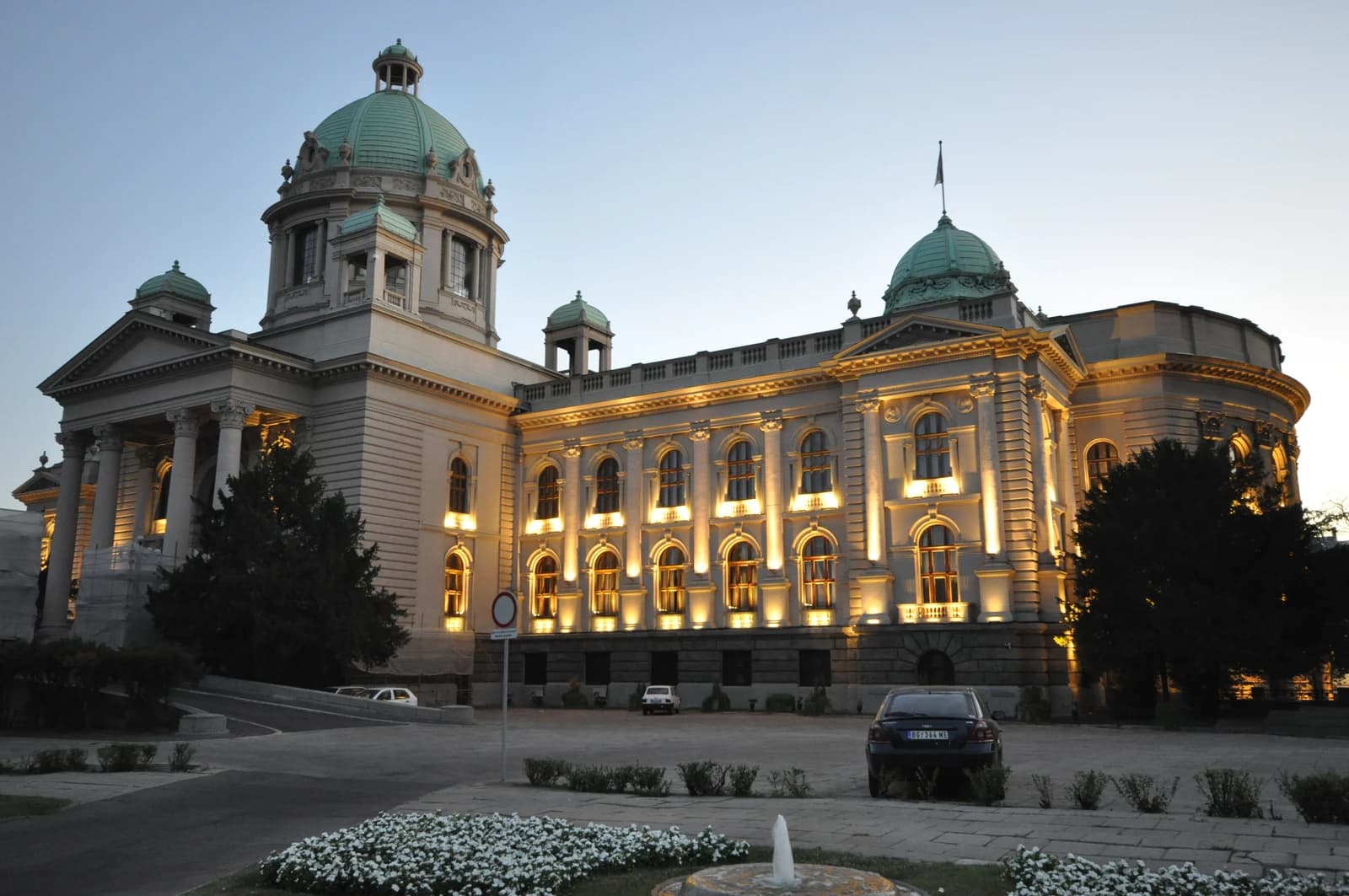 The Serbian National Assembly Building in Belgrade at twilight, with lights illuminating its facade.