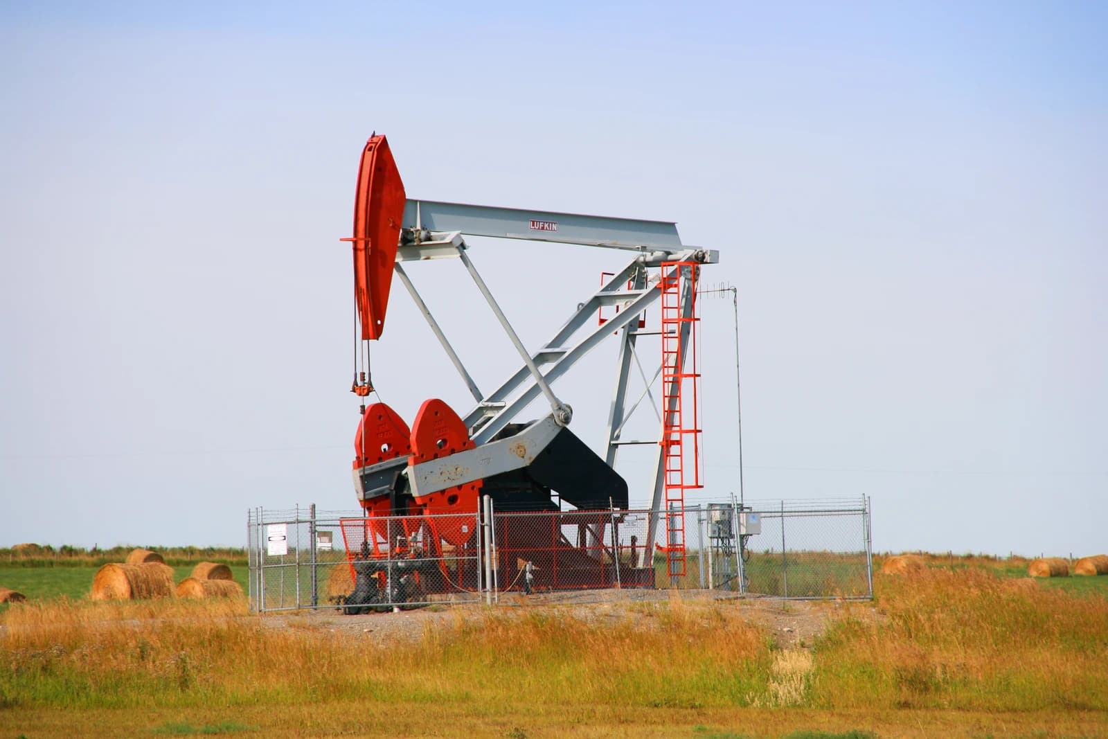 A red and grey pumpjack in operation in a field under a clear sky.