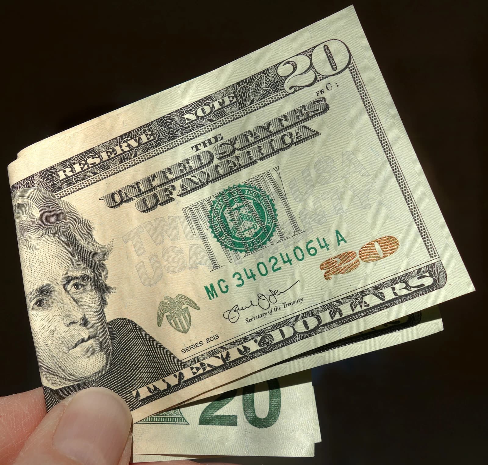 Hand holding several folded twenty dollar US banknotes.