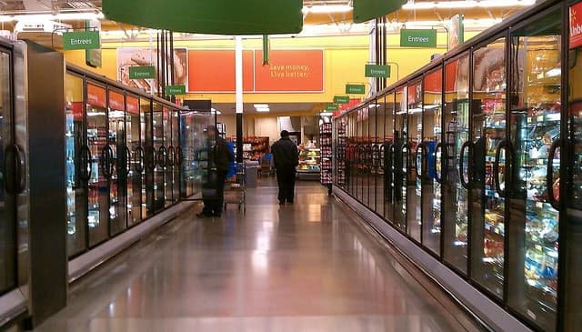 Walmart frozen foods aisle with shoppers and "Save money. Live better." sign.