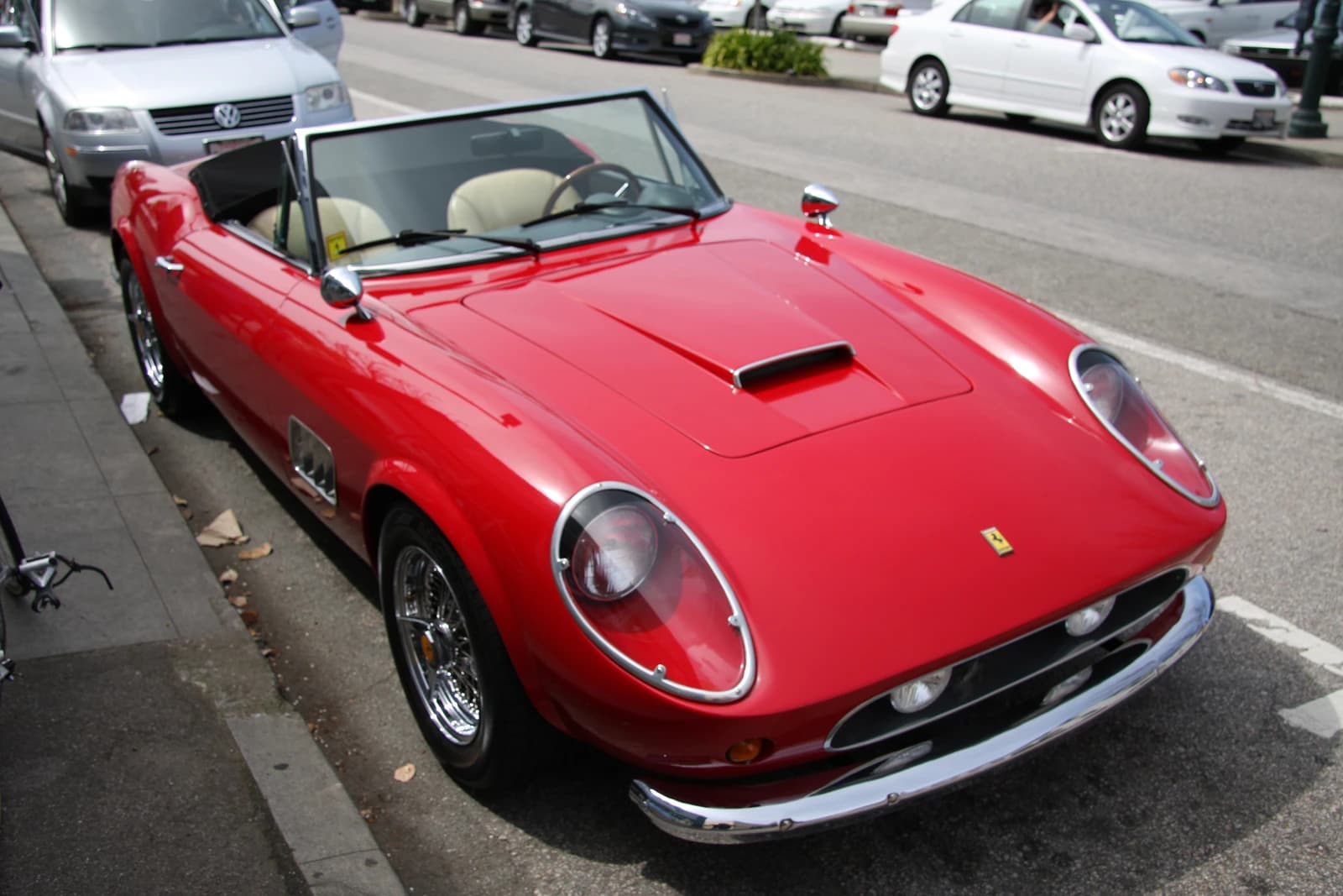 Red Ferrari 250 GT California Spyder convertible parked on the side of a street.