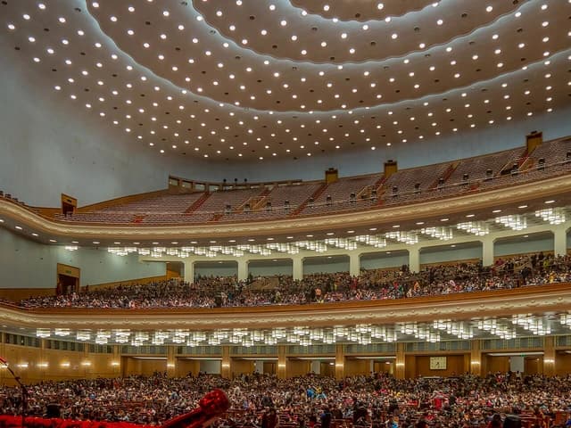 A large, multi-tiered auditorium filled with people under a brightly lit domed ceiling.