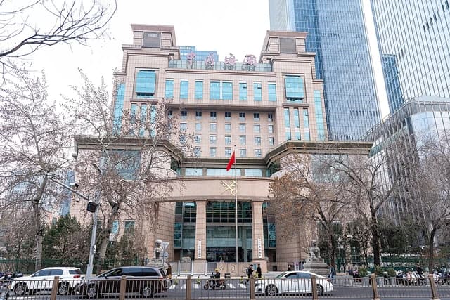 Beijing Customs Building with a red Chinese flag flying at its entrance on a cloudy day.
