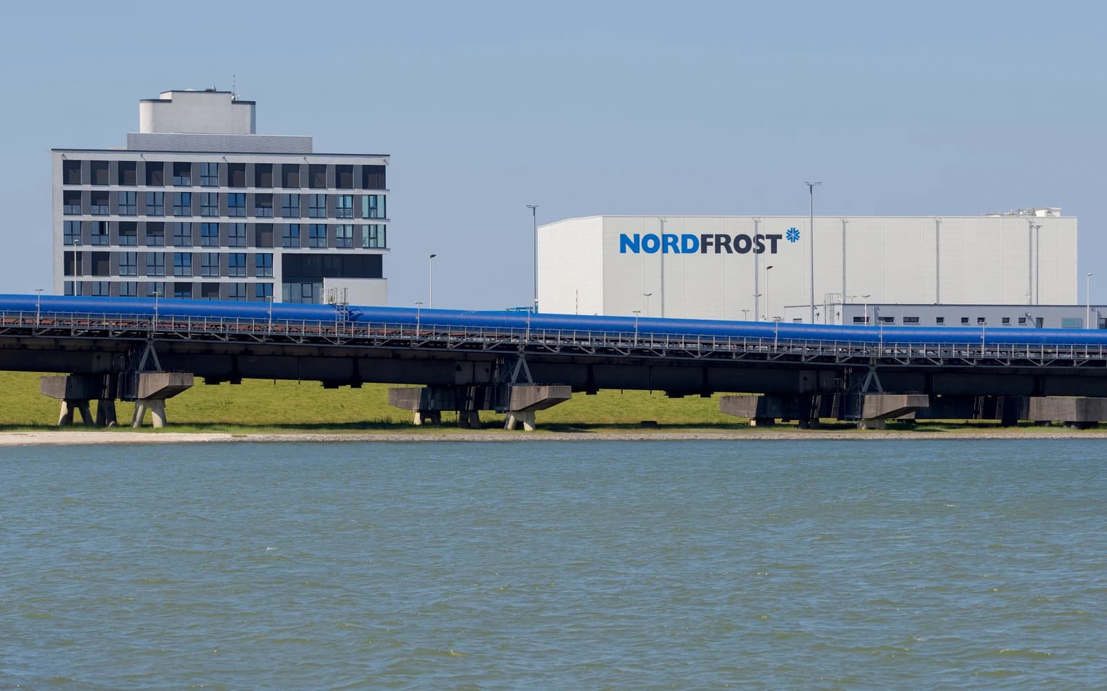 Blue gas pipeline stretching over a body of water next to industrial buildings.