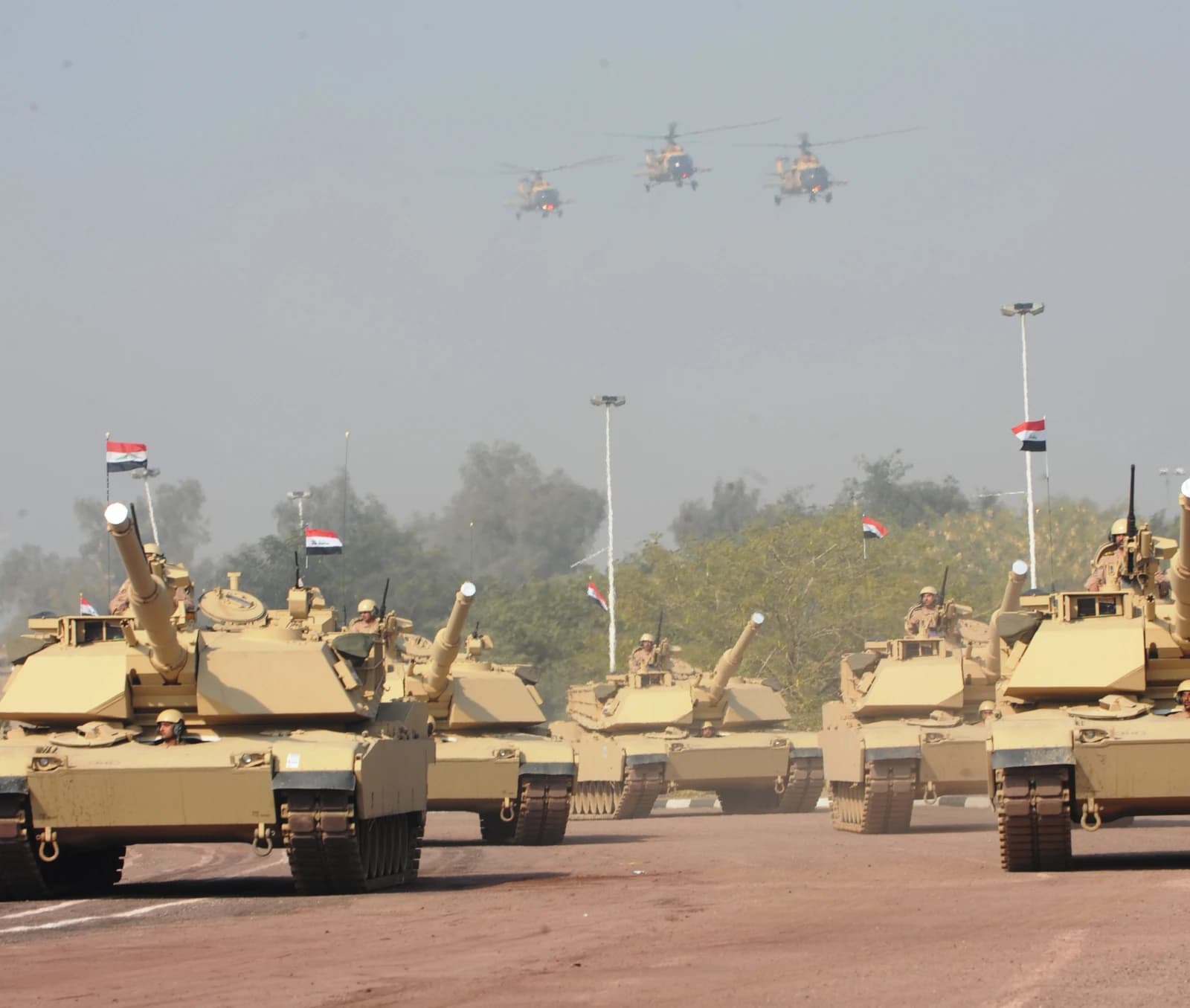 M1 Abrams tanks from the Iraqi army move in formation with helicopters above.
