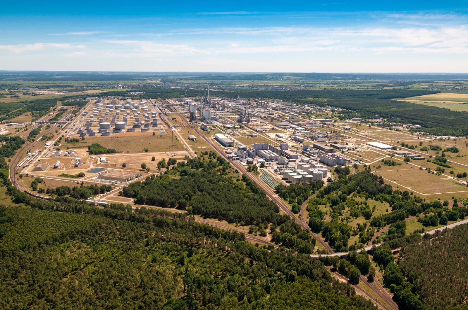 Aerial view of the sprawling PCK Schwedt refinery, surrounded by green landscape under a blue sky.