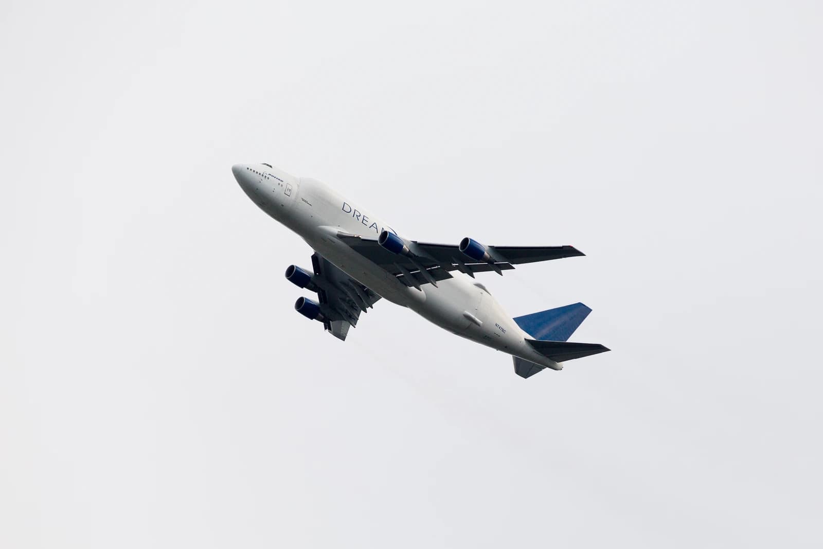 Boeing Dreamlifter, a modified 747 freighter, ascends into a light gray sky.