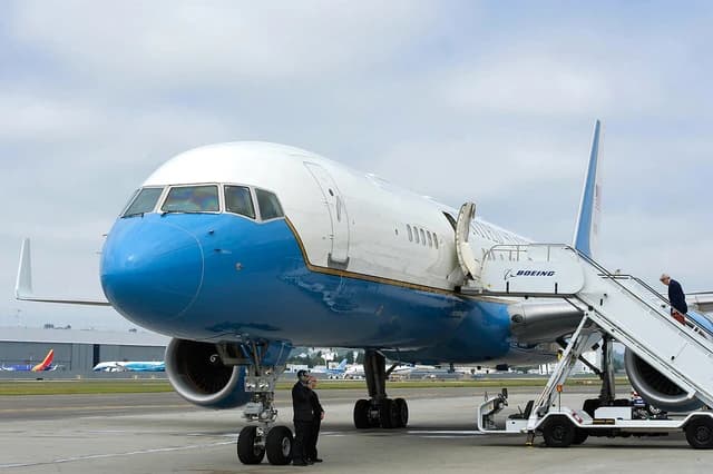 Secretary Kerry boards a blue and white Boeing C-32A airplane at an airfield.