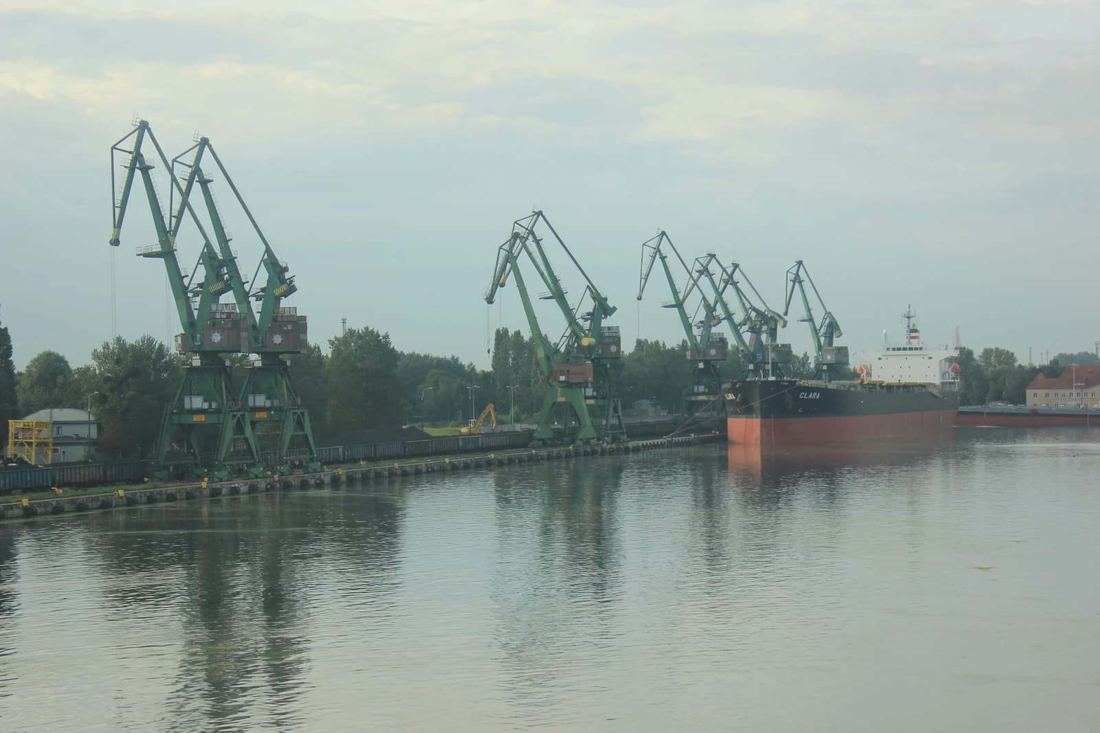 Industrial cranes and a large cargo ship at a port facility with piles of coal visible.