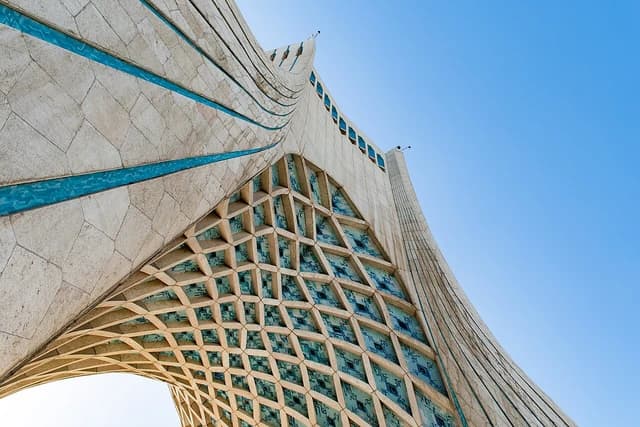 Architectural detail of Azadi Tower in Tehran, showing geometric patterns and a clear blue sky.