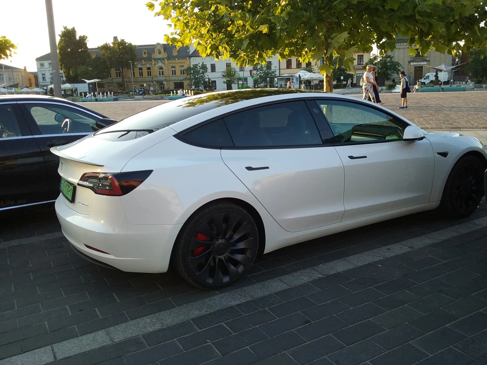 A white Tesla Model 3 Dual Motor car parked on a brick street.