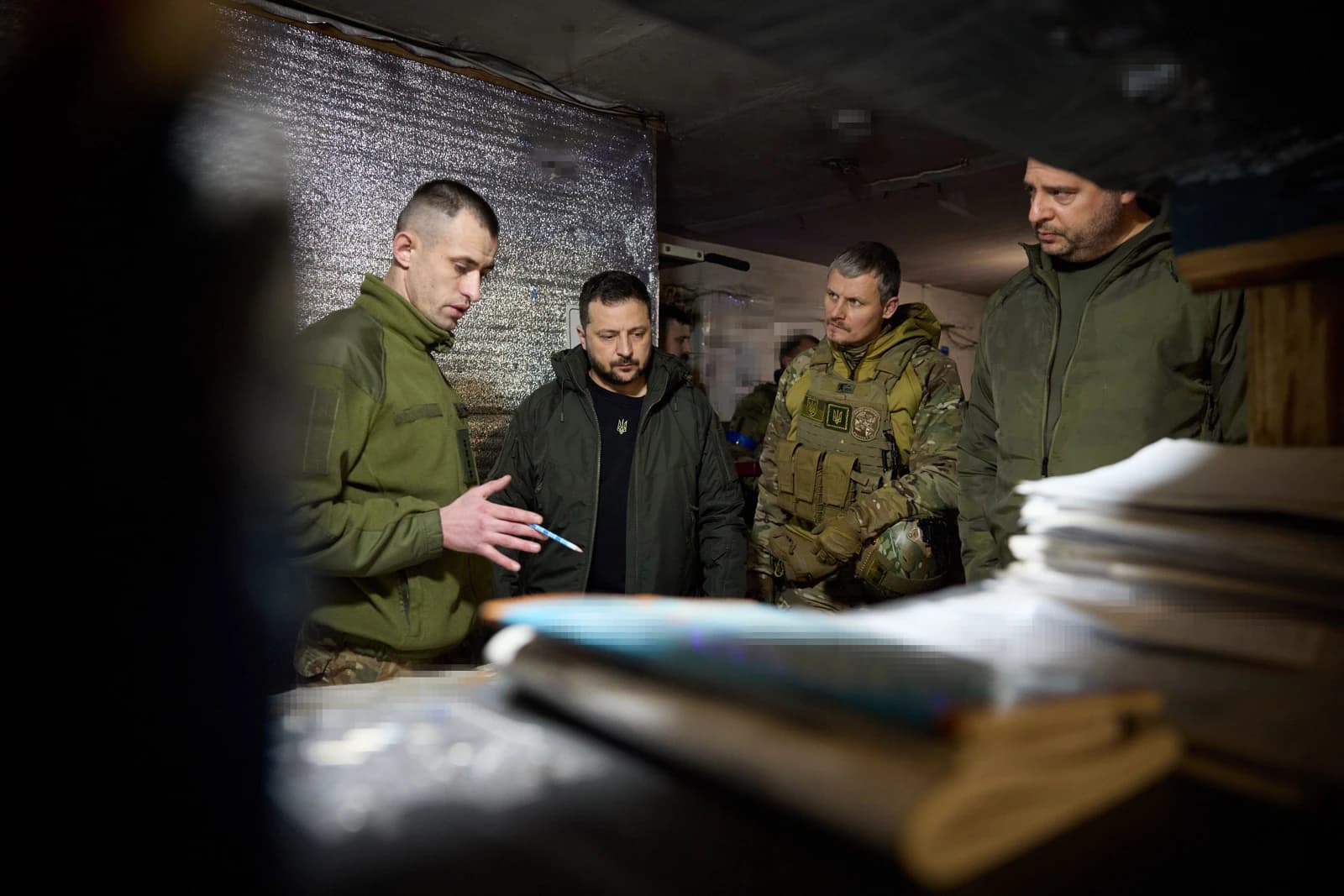 Volodymyr Zelenskyy, President of Ukraine, stands with military personnel indoors.