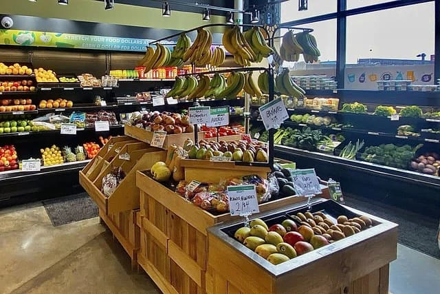 Colorful fruits and vegetables including bananas, apples, pears, avocados, and kiwi displayed in a grocery store.