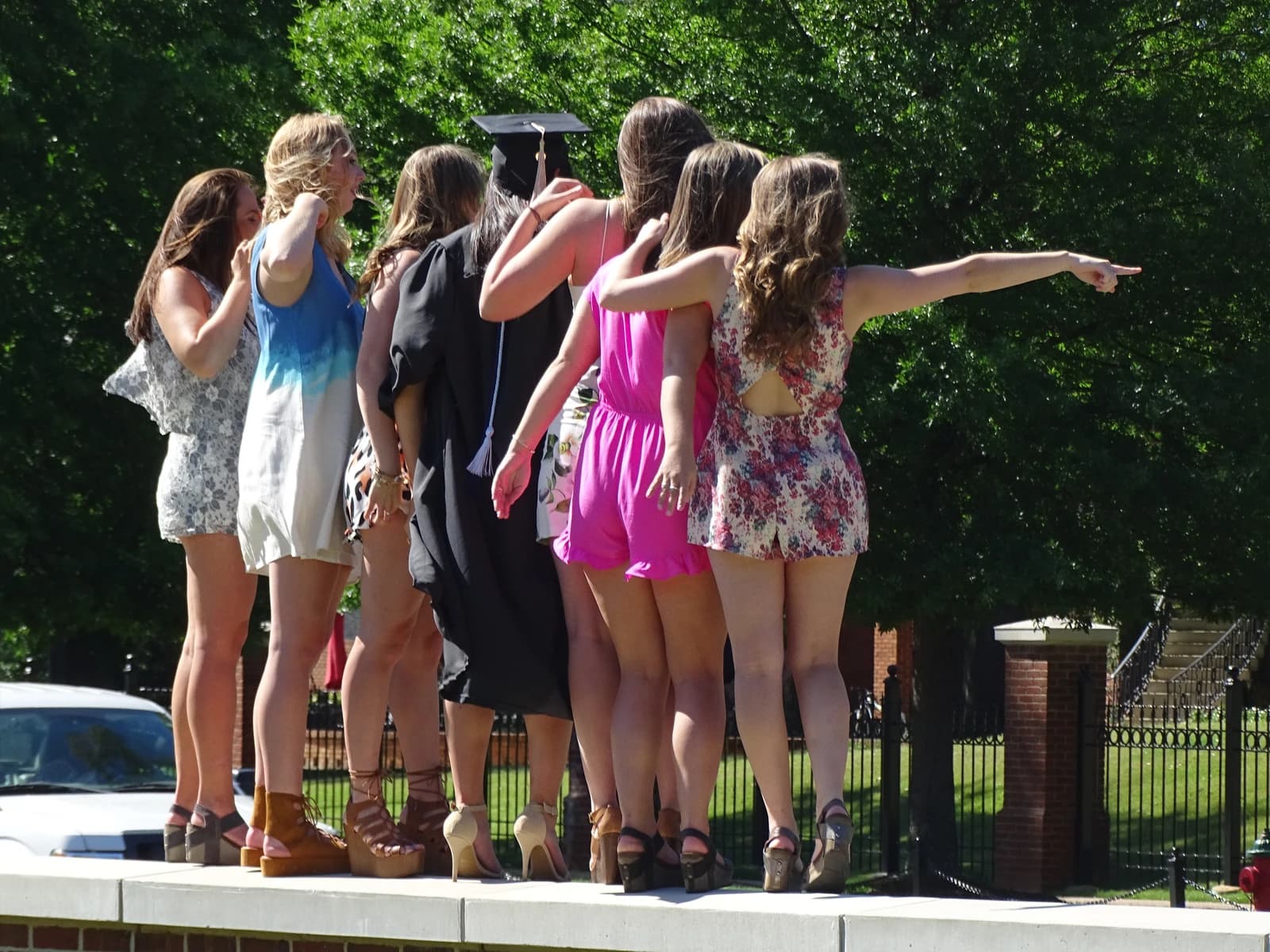 Female students, one wearing a graduation cap, are standing outdoors and looking right.