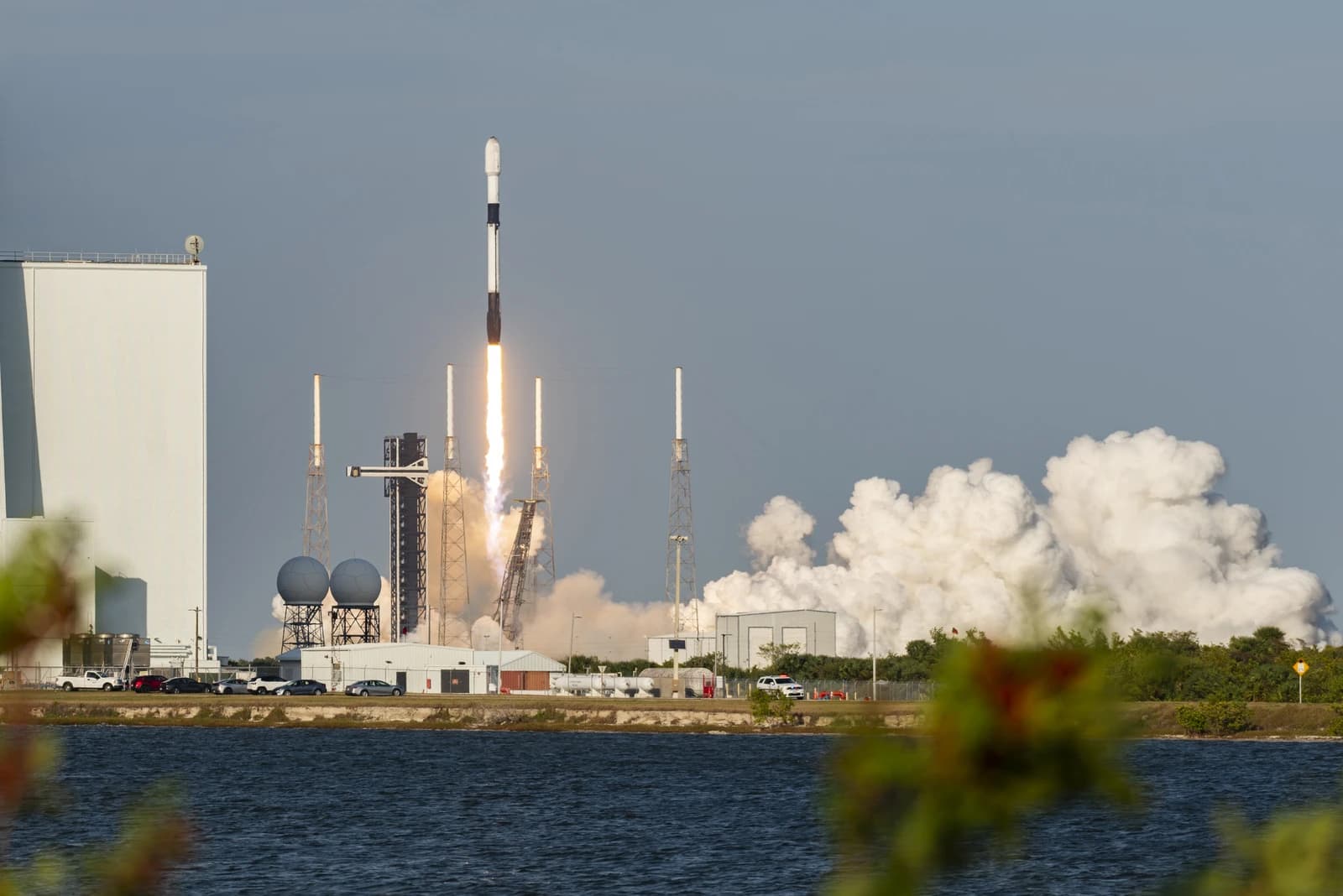 A Starlink rocket launches from a coastal facility with bright exhaust and smoke.