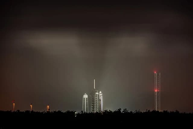 SpaceX Falcon 9 rocket and launch tower on pad at Kennedy Space Center at night.