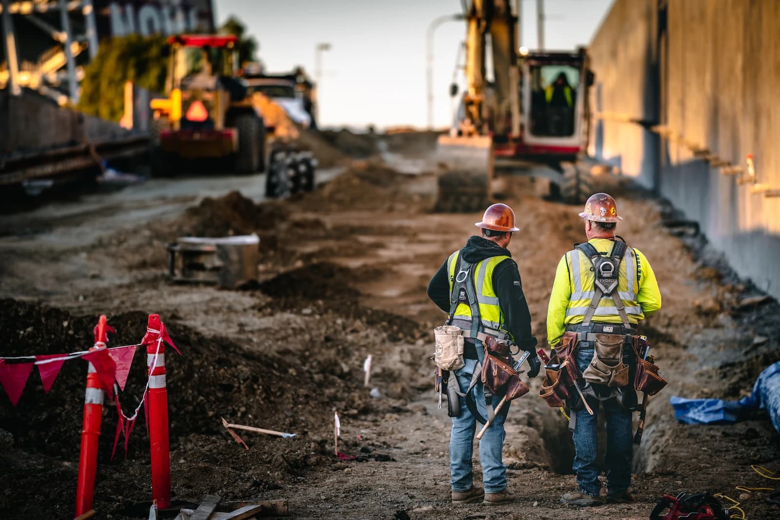 Two construction workers in hard hats and safety vests standing at a construction site.
