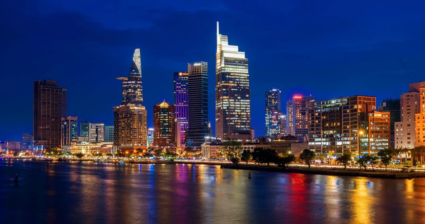 Ho Chi Minh City skyline at night with multiple illuminated high-rise buildings along a river.