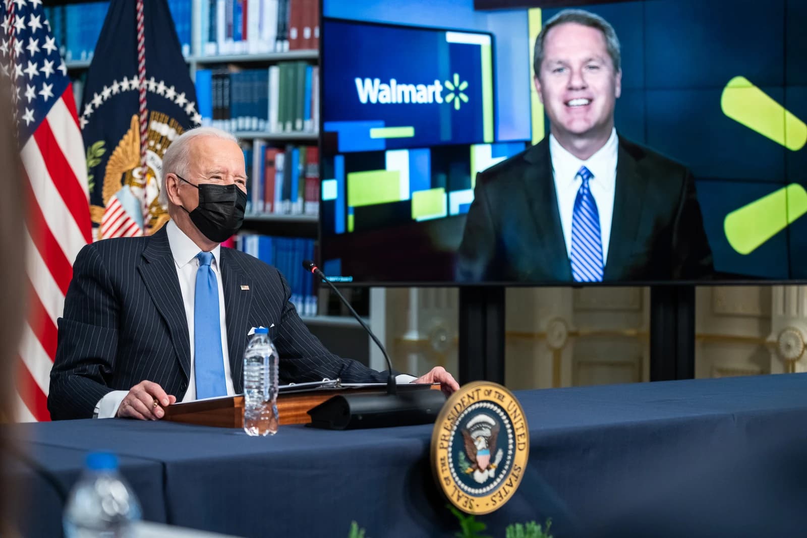 President Biden, wearing a black mask, seated at a table with a Walmart executive on a screen.