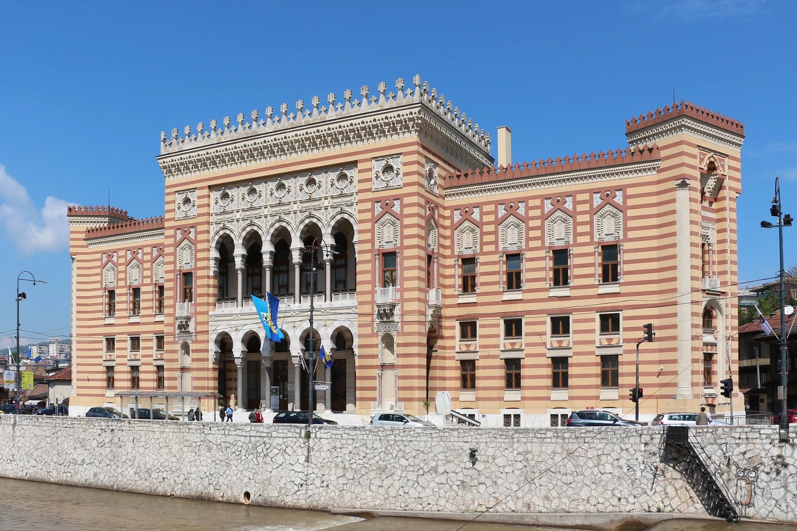 Sarajevo City Hall, a prominent building with red and white striped facade, next to a river.