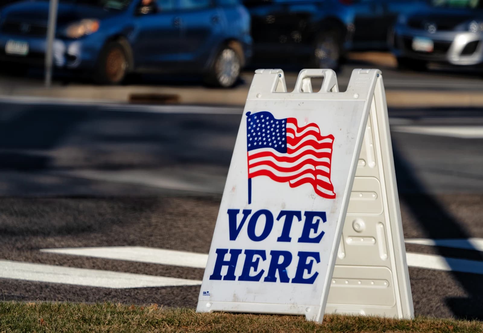 White sandwich board sign with an American flag and 'Vote Here' text.