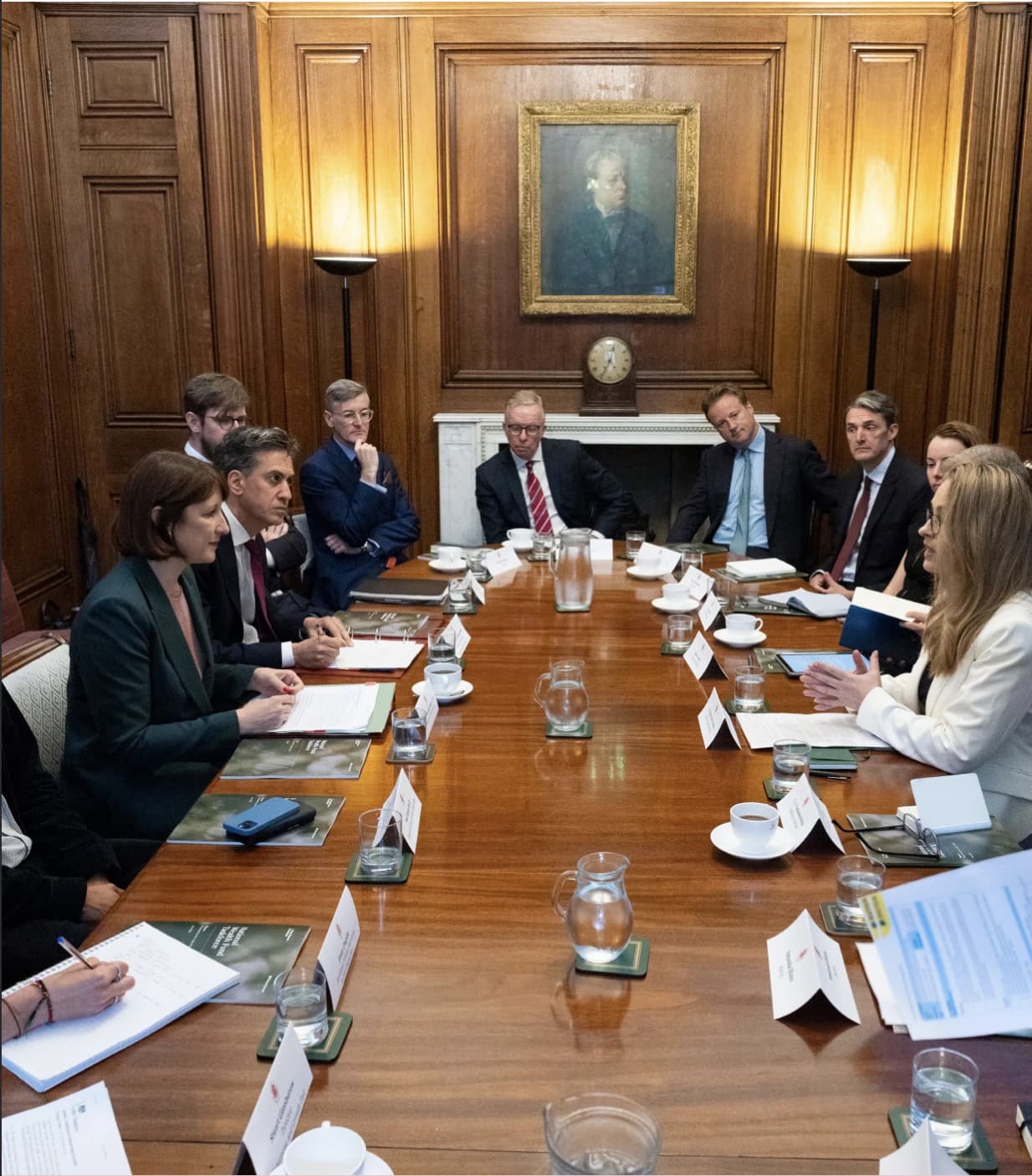 Members of a government task force sitting around a large wooden conference table.