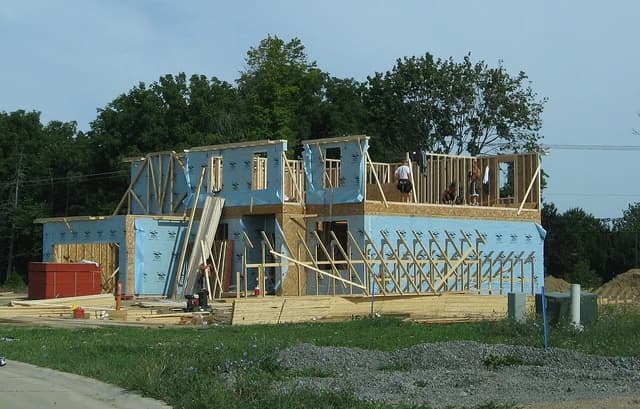 New house under construction with visible wooden framing and blue weather barrier in Michigan.