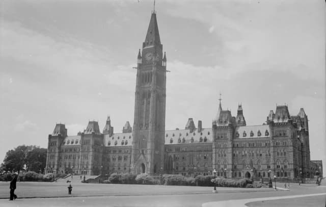 The Parliament Building in Ottawa, Canada, viewed from a distance with a large lawn.