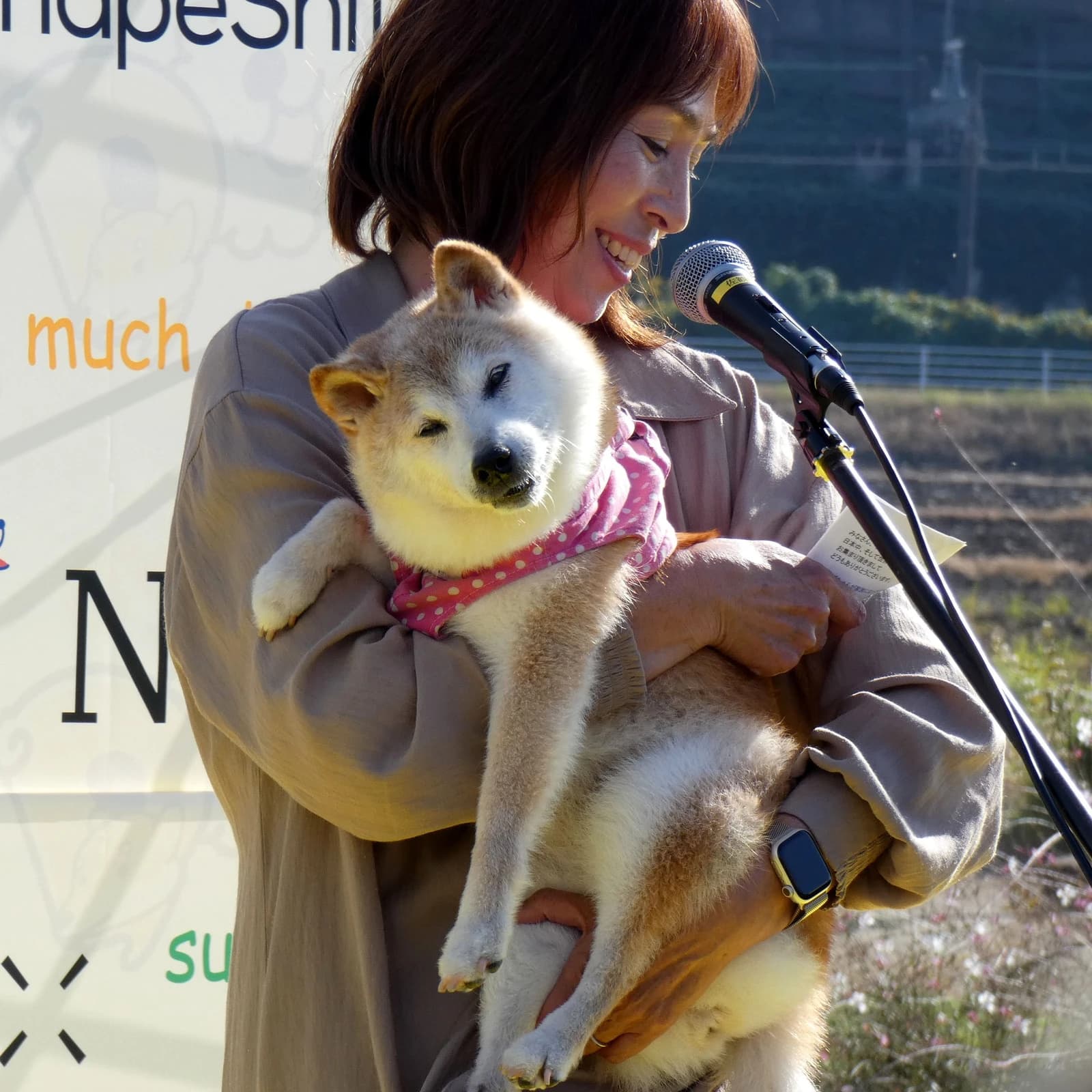 Atsuko Sato, owner of Kabosu, holding the Shiba Inu dog at an outdoor event.